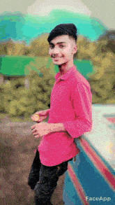 a young man wearing a pink shirt is leaning against a wall and smiling