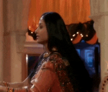 a woman with long black hair is standing in a room wearing a saree .