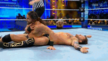 two men are wrestling in a wrestling ring and one is laying on the floor .