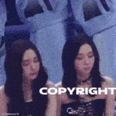 two women are sitting next to each other in front of a sign that says copyright