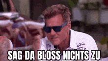 a man wearing sunglasses and a white shirt is making a funny face and saying `` sag da bloss nichts zu '' .