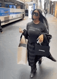 a woman wearing sunglasses and a chanel bag walks down a street
