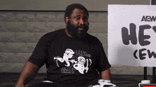 a man sitting in front of a sign that says " he 's crew "