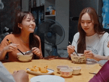 two girls are sitting at a table with bowls of food and one has a shirt that says " i love rice "