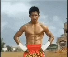 a boxer without a shirt is standing with his hands on his hips in a field .