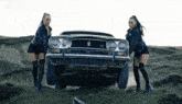 two women standing next to a car that has the letter r on the front