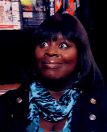 a woman in a black jacket and blue scarf smiles for the camera