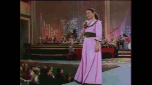 a woman in a pink dress sings into a microphone
