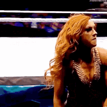 a woman with red hair is standing in a wrestling ring looking to the side .