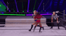two women are wrestling in a wrestling ring while a referee watches .