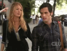 a man and a woman are walking down a street and the man is wearing a plaid shirt that says cw on it