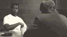 two men are sitting at a table talking to each other in a room .