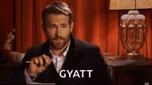 a man with a beard is holding a pen and the word gyatt is on the screen