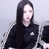 a woman wearing a black adidas jacket with white stripes