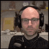 a bald man wearing headphones and glasses is making a funny face .