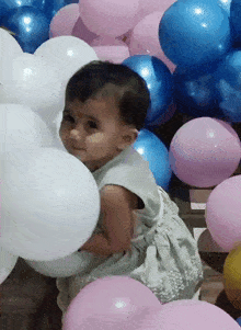 a baby in a white dress is surrounded by balloons