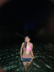 a woman in a pink bikini and blue shorts stands in the water at night