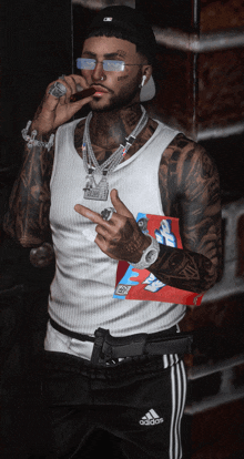 a man wearing a white tank top and black adidas pants smoking a cigar