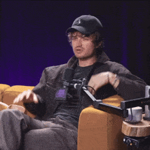a man wearing a hat with the letter s on it sits in a chair with a microphone