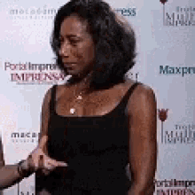 a woman in a black tank top is talking to another woman in front of a white wall .