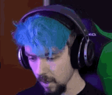 a man with blue hair and headphones is sitting in a green chair .