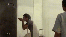 a man is taking a shower in a bathroom while another man stands behind him .