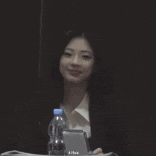 a woman in a suit sits at a table with a bottle of water and a phone that says kitsa on it