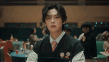 a young man wearing a vest and tie is sitting at a table in a restaurant .
