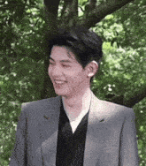 a young man in a suit and black shirt is smiling in front of trees .