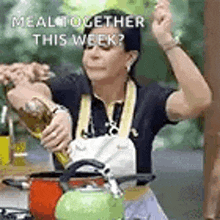 a woman in an apron is pouring a bottle of liquid into a pot .