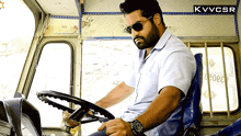 a man wearing sunglasses sits in the driver 's seat of a vehicle that says kvvcsr on the bottom