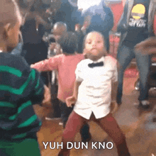 a boy in a bow tie is dancing in a crowd with the words yuh dun kno behind him
