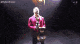 a man in a purple suit holds a microphone and a wrestling belt