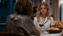 a woman sits at a table with a glass of wine