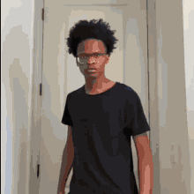 a young man wearing glasses and a black shirt is standing in front of a white door .