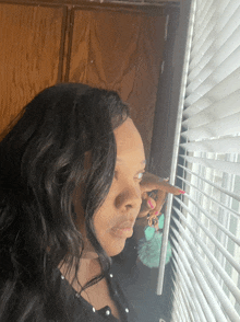 a woman looks out of a window with blinds on