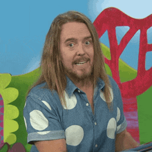 a man with long hair and a beard wearing a polka dot shirt is smiling .