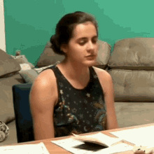 a woman in a black tank top is sitting at a table with a book .