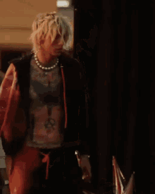 a man with blonde hair and a pearl necklace walks down a street