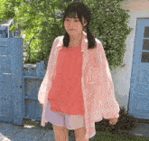 the girl is wearing a pink shirt and shorts and is standing in front of a blue fence .