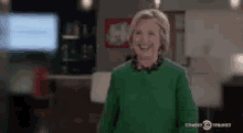 a woman wearing a green sweater is smiling in a room .