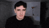 a man in a black shirt is making a funny face in a living room with a lamp in the background .