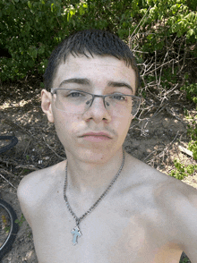 a shirtless young man wearing glasses and a cross necklace takes a selfie