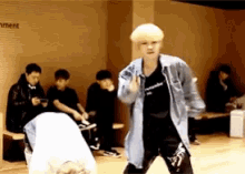 a man in a denim jacket is dancing in front of a group of people sitting on benches .