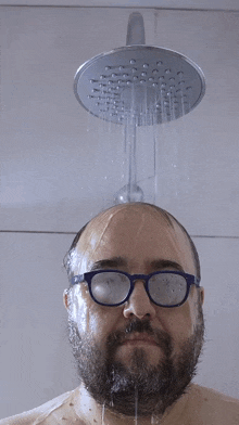 a man with glasses is taking a shower and the water is coming out of the shower head