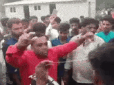 a group of people are standing around a man in a red shirt holding a rope around his head .