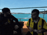 two men are sitting on a boat and one of them is wearing a shirt that says ok