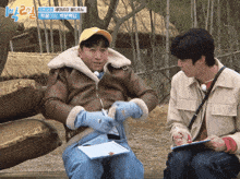 a man in a leather jacket is sitting next to another man in a yellow hat