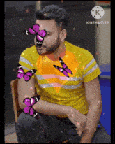 a man in a yellow shirt is surrounded by purple butterflies and the words kinemaster on the bottom
