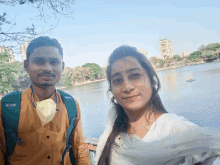 a man and a woman pose for a picture in front of a body of water